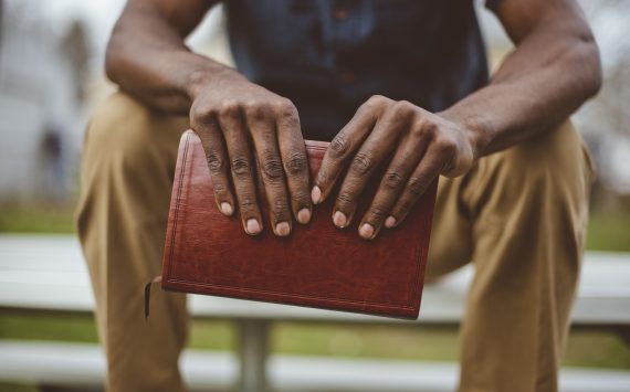 A closeup shot of a male sitting in the park while holding the bible with a blurred background